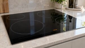 A built-in black glass electric cooktop set into a stone countertop with a short error code lit on its touch control strip