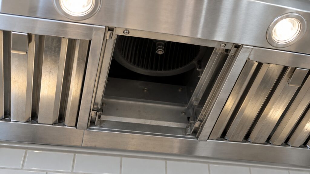 The underside of a hood liner with one stainless baffle filter removed, showing the empty filter channel and the blower opening above it