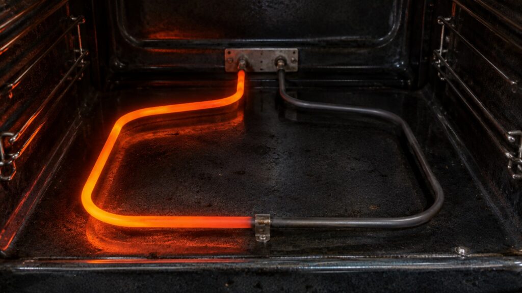 A close-up of a bake element in an oven cavity, half of it glowing orange and half still dark