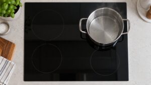 A black glass induction cooktop with a stainless pot of water that is barely steaming on one zone, seen from above
